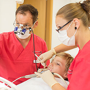 Zahnarzt behandelt mit Assistentin einen jungen Patienten