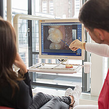 Zahnarzt zeigt Patientin einen Zahn auf Bildschirm