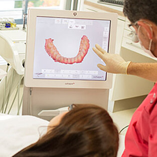 Zahnarzt zeigt Patientin ein Gebiss am Bildschirm
